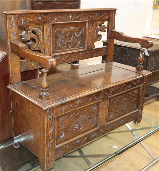 An 18th century style carved and panelled oak monks bench W.100cm